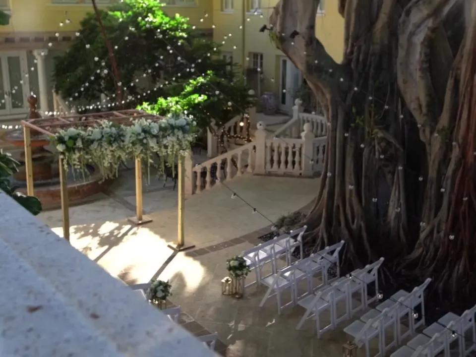 Allée de cérémonie extérieure avec chaises blanches, arche fleurie et guirlandes lumineuses